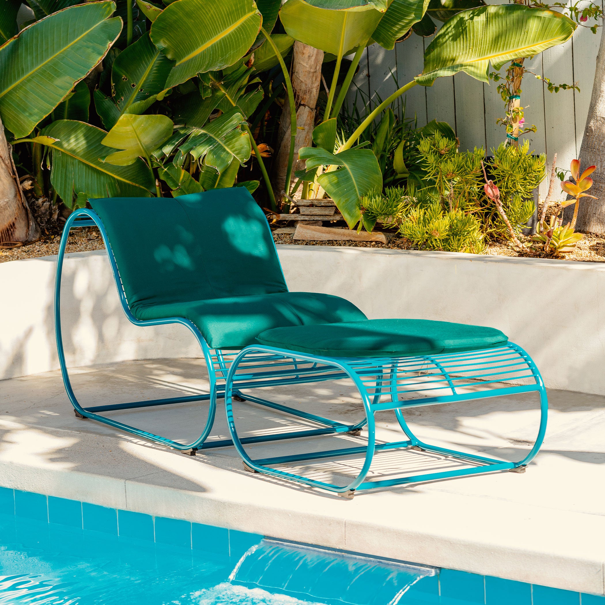 Loop Lounge Chair and Ottoman shown in Peacock Blue with Forest Green Sunbrella Padding. Pictured sitting poolside on Summer Day