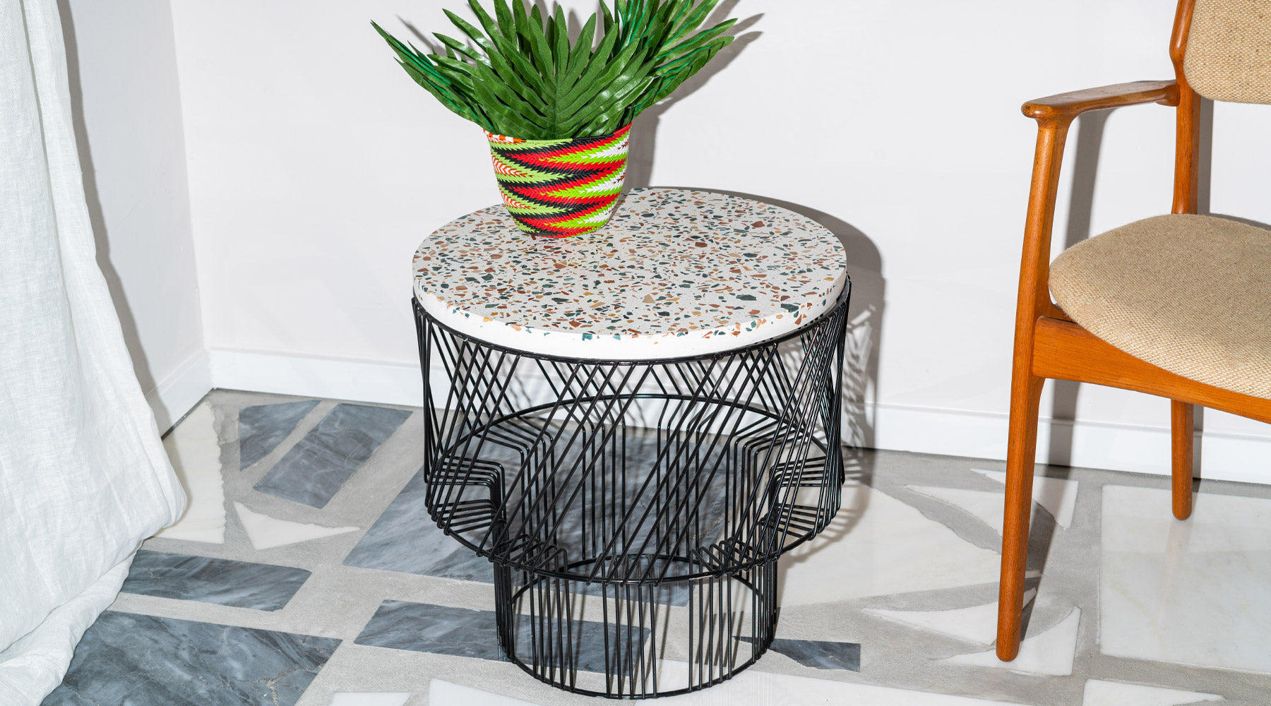 Close up of Terrazzo Side Table in Black. Pictured in interior space next to mid-century chair.