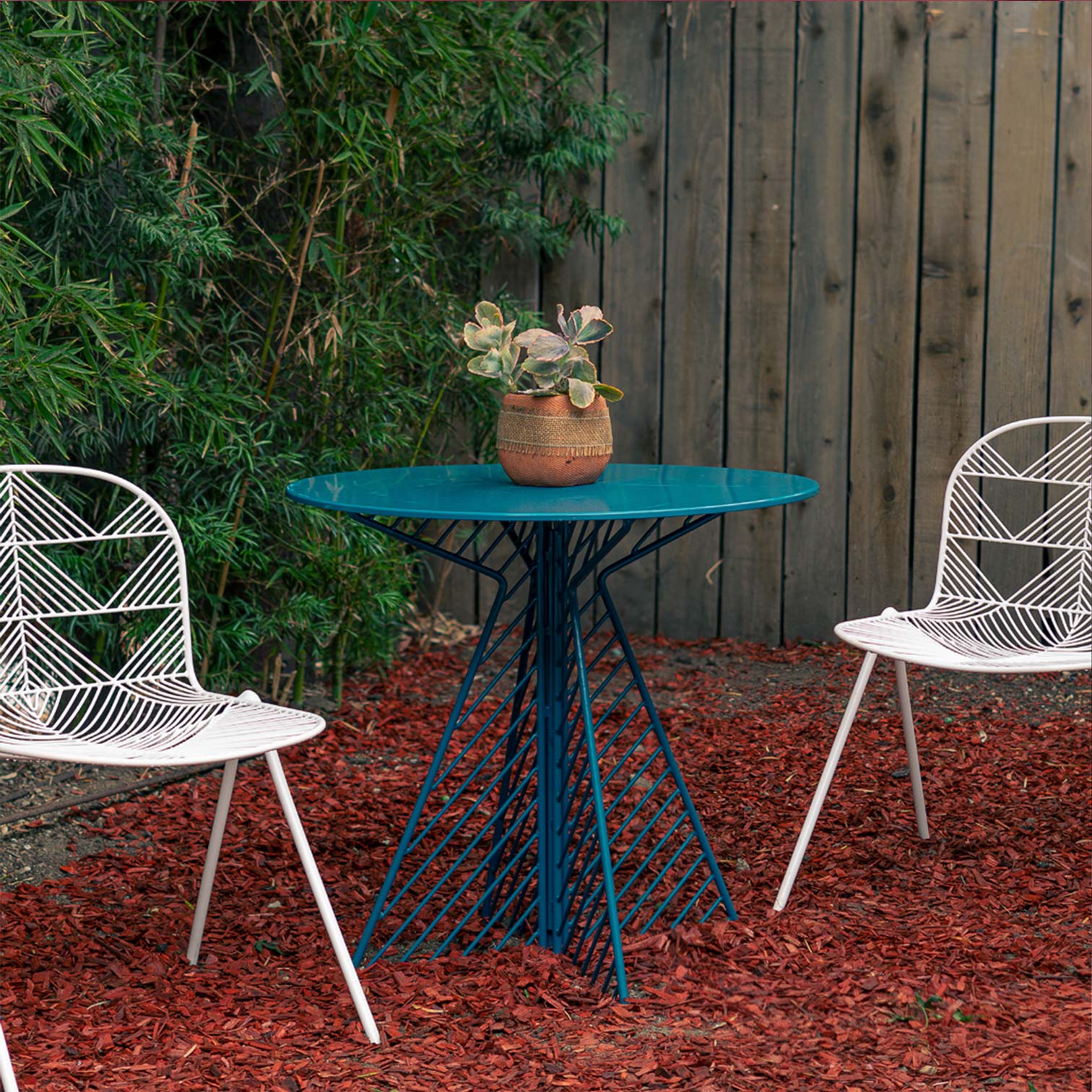 Cafe Table shown in Peacock Blue. Pictured outdoors alongside two Betty Stacking Chairs in backyard of Los Angeles home.