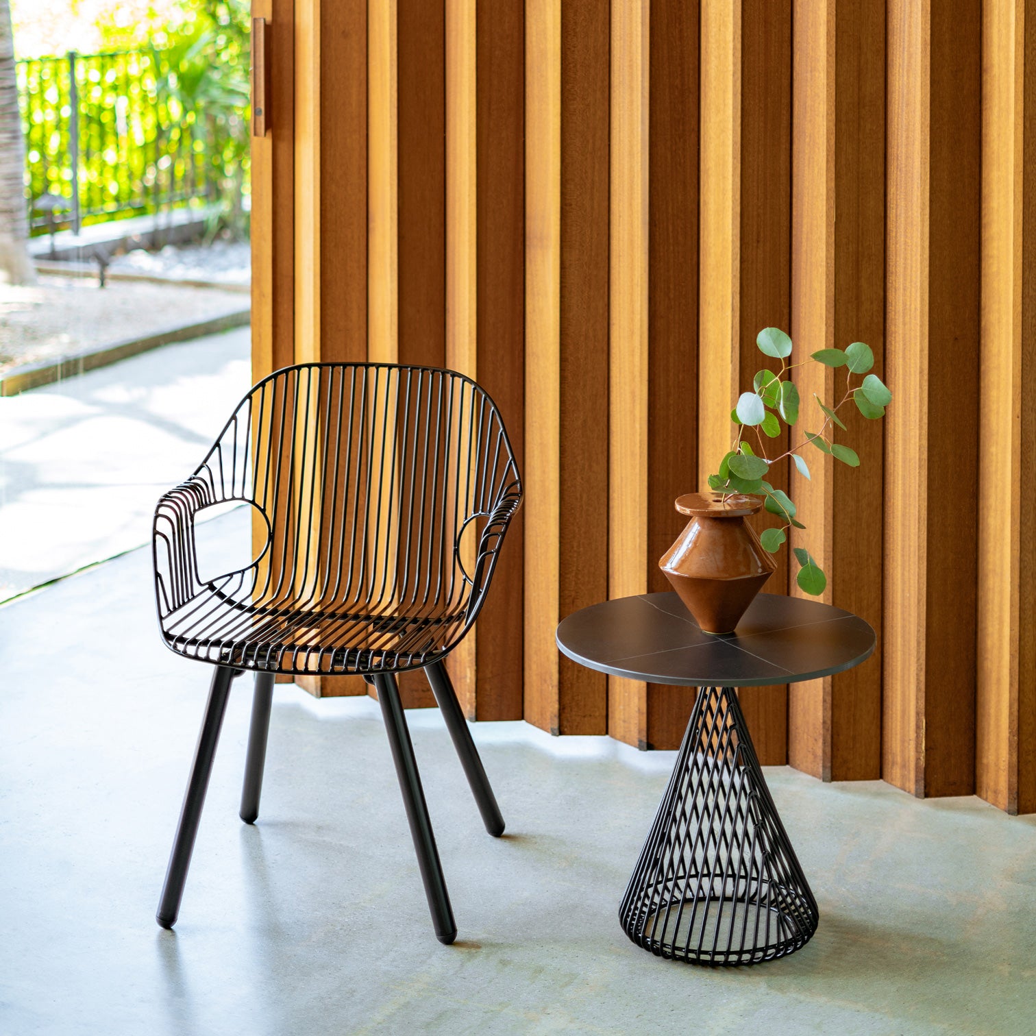 Cono Table shown in Black with Black Ceramic Stone Top. Pictured next to the Rita Arm Chair.