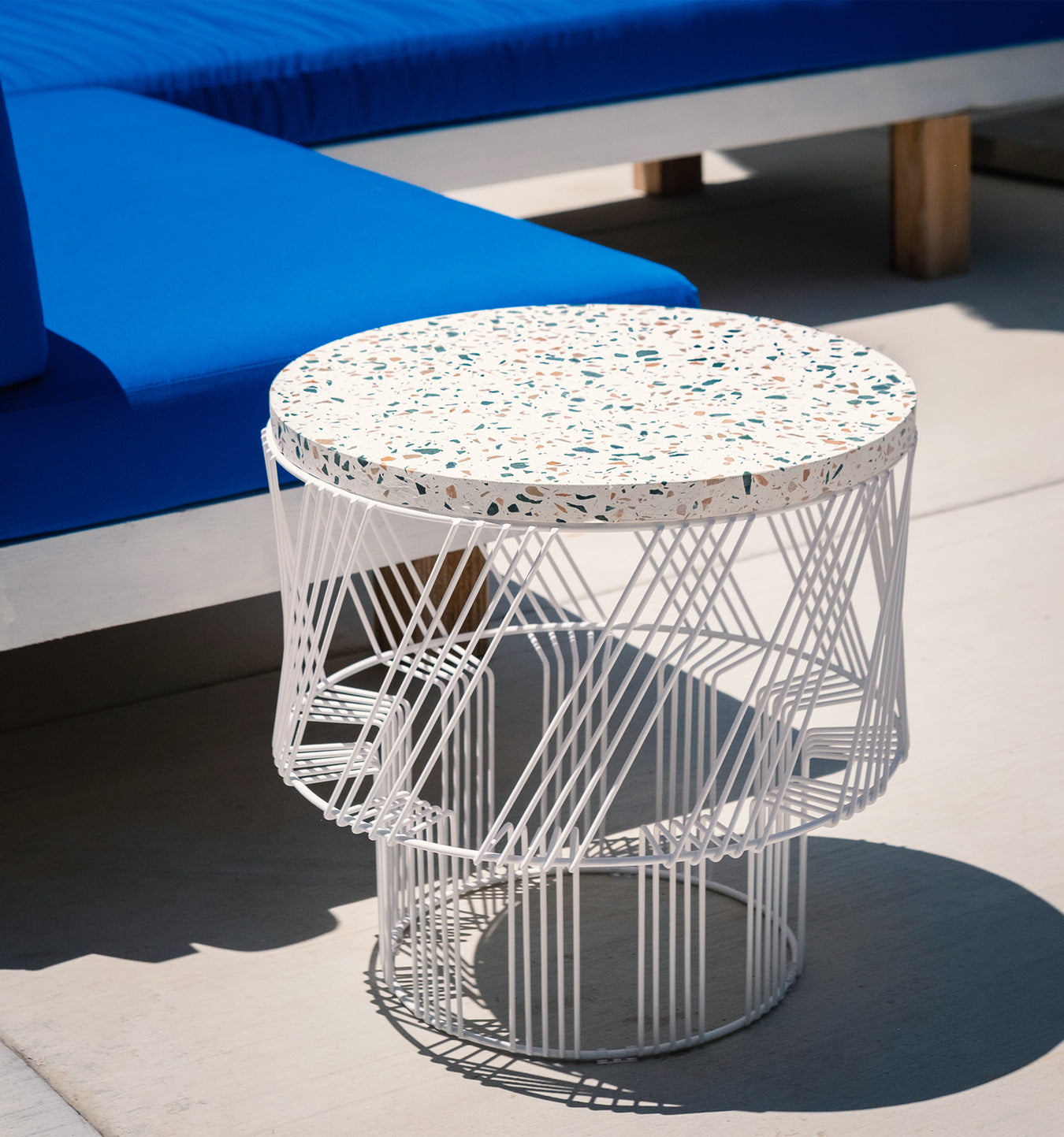 Terrazzo Side Table shown in White. Pictured outdoors next to poolside sofa.
