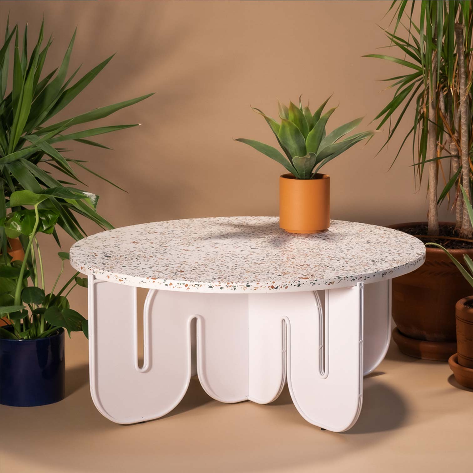 Wave Table shown in White with Terrazzo Stone Top. Pictured in front of tan backdrop surrounded by house plants.