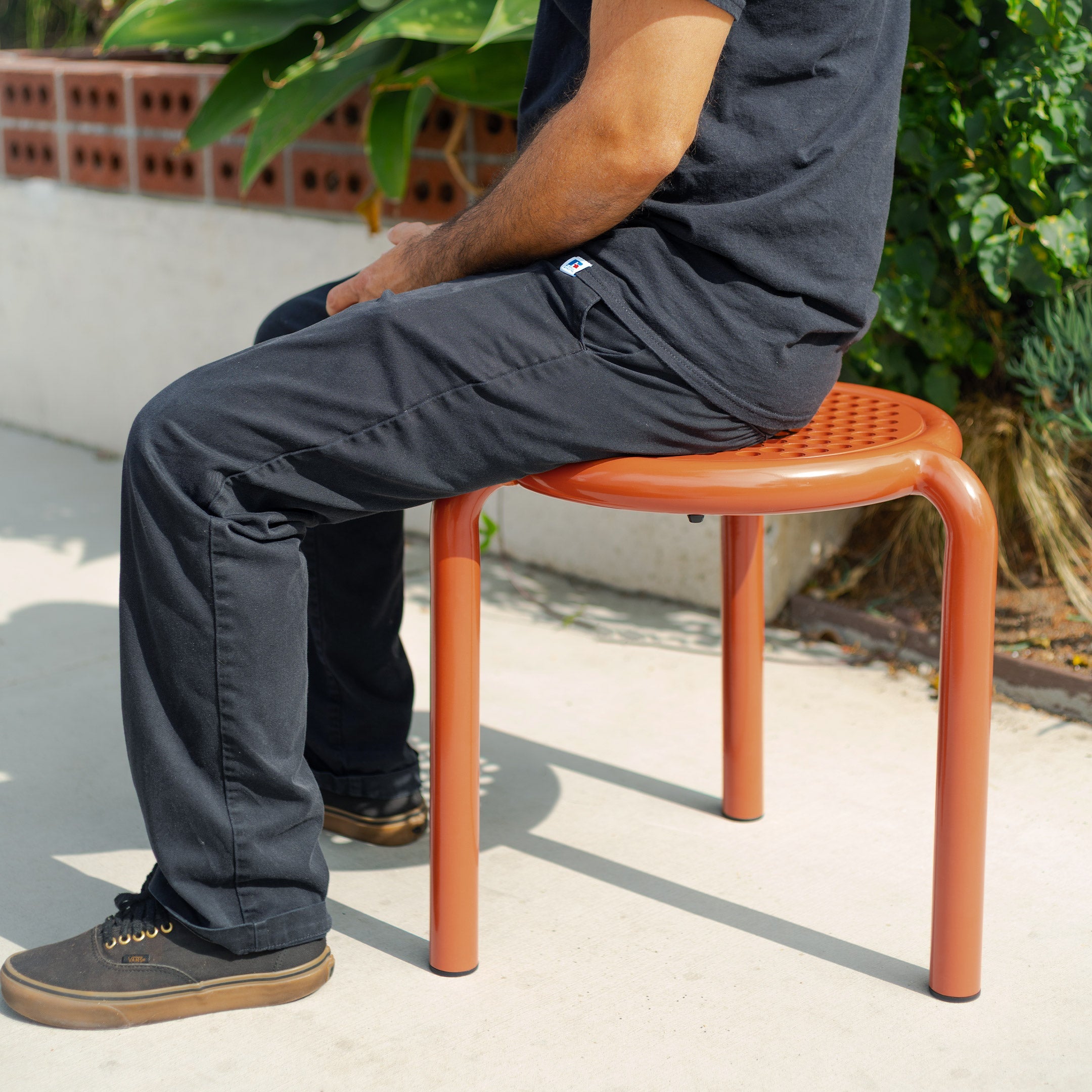 The signature Lucy Stool in Orange nestled up to a kitchen counter. The Lucy Stools are a wire design made for both outdoor and indoor dining.
