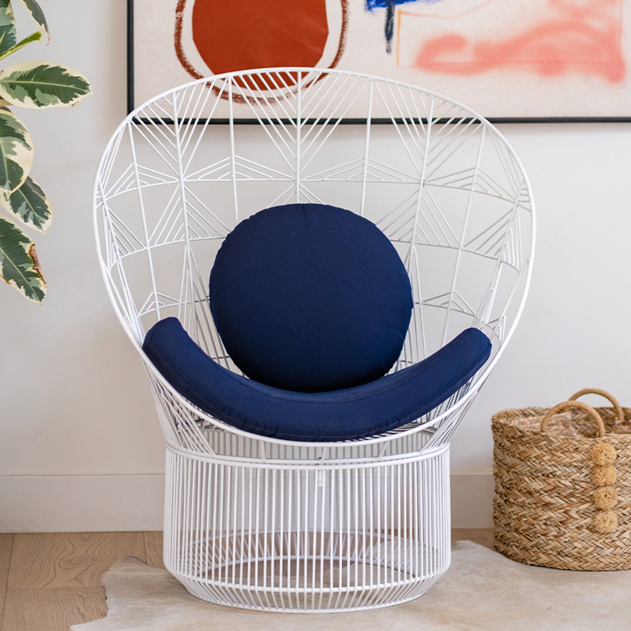 The Peacock lounge chair is a wire chair design made for both outdoor patio sets and indoor living room furniture. sisplayed here is the White lounge chair next to a fireplace in a modern home.