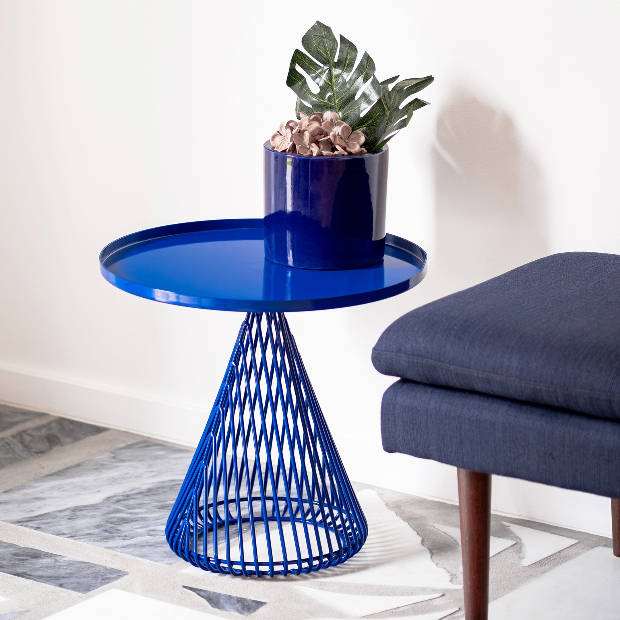 Cono Table shown in Electric Blue. Pictured next to ottoman seat in interior space with grey tiles.