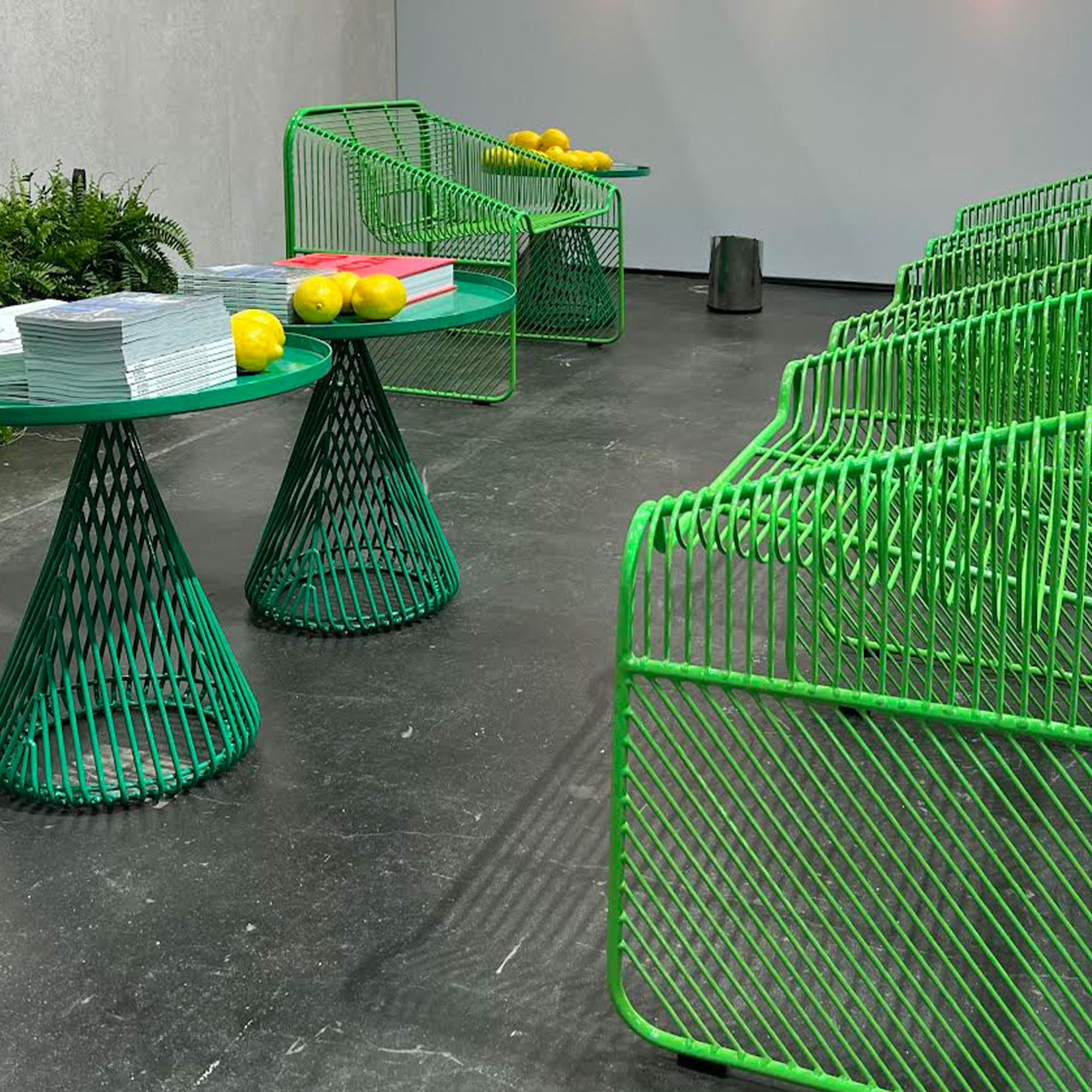 Modern green wire furniture set including chairs and tables on a gray floor.