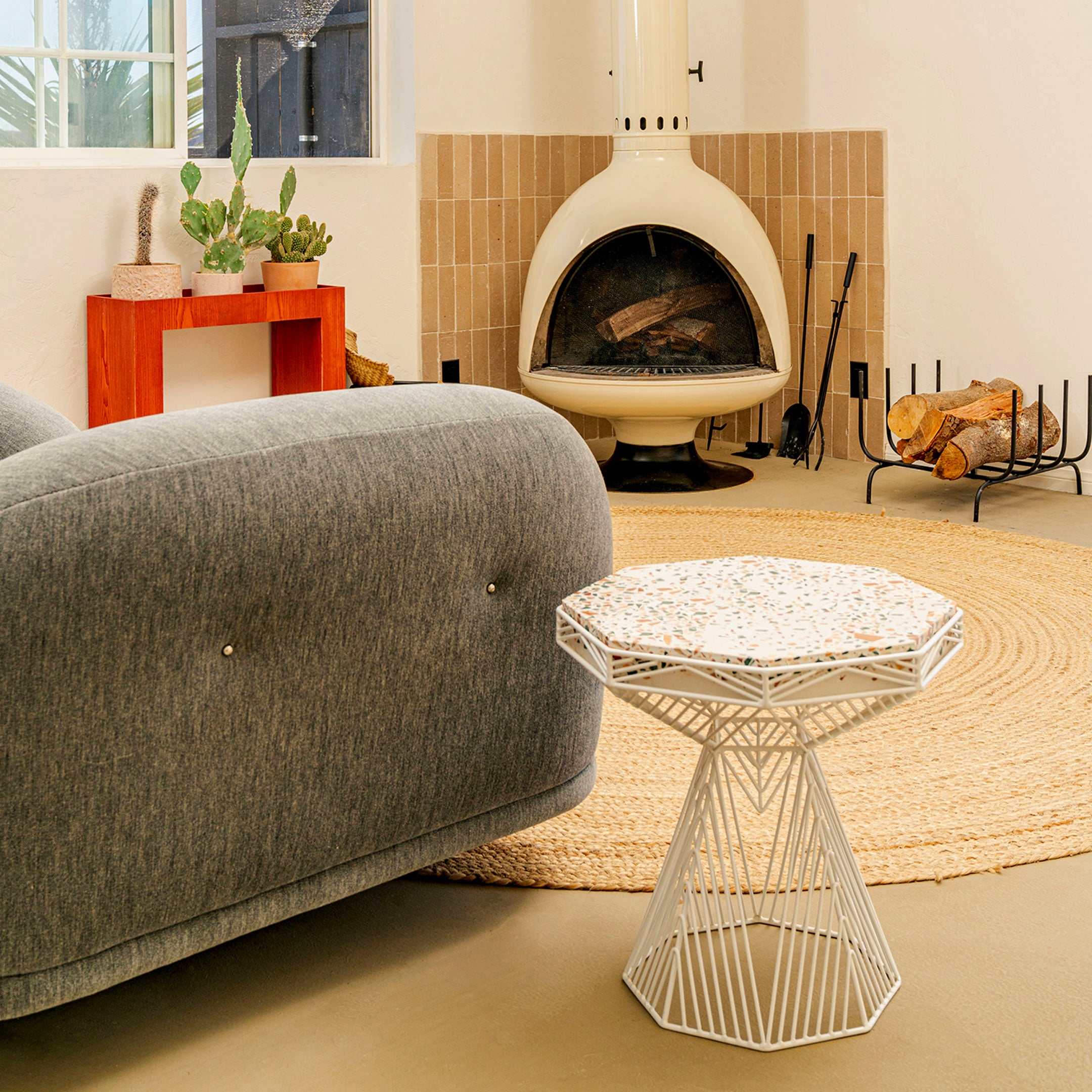 Terrazzo Switch Table shown in White. Pictured next to a sofa and near the fire place in interior room.