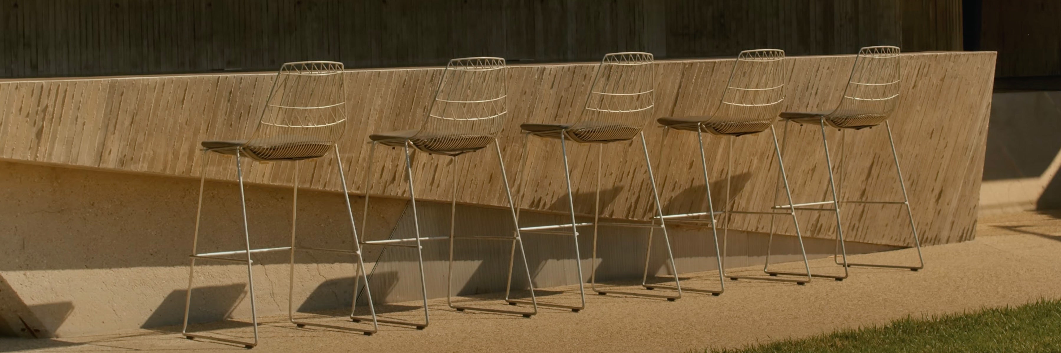 Row of metal lucy bar stools against a concrete bartop wall.