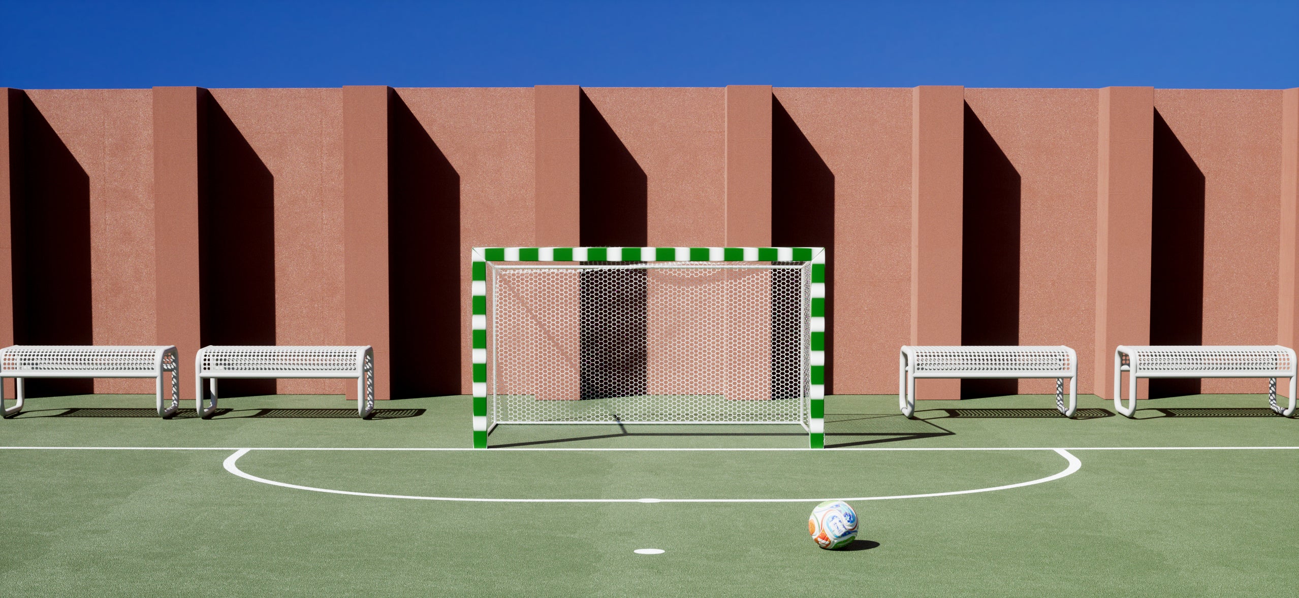 Bend Goods Tube Bench on a soccer field, modern outdoor aluminum seating for parks, stadiums, hospitality projects, and public gathering spaces