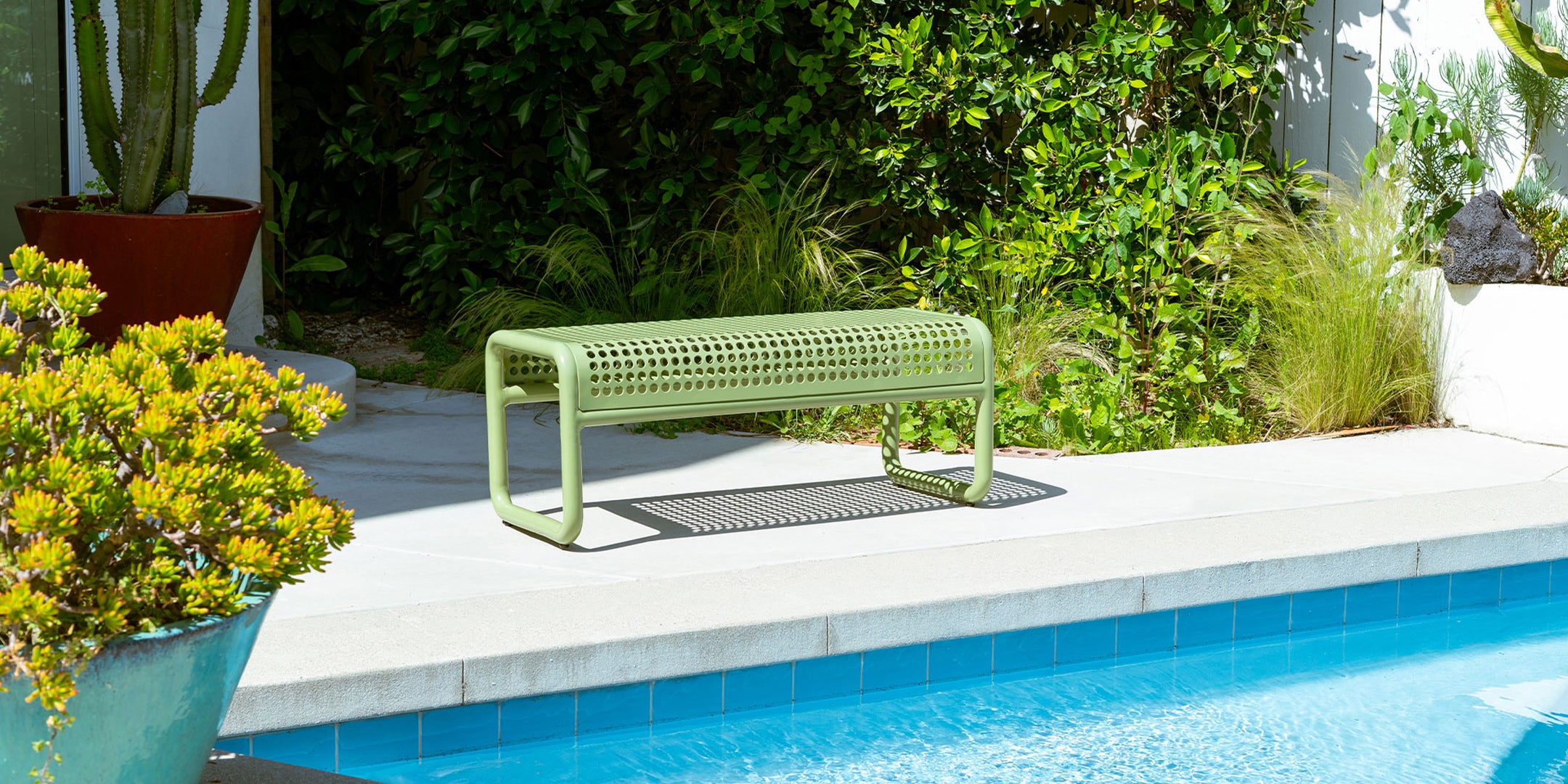 Green bench by a pool with plants and a cactus in the background. Tube Bench Indoor & Outdoor Perforated bench from Bend Goods